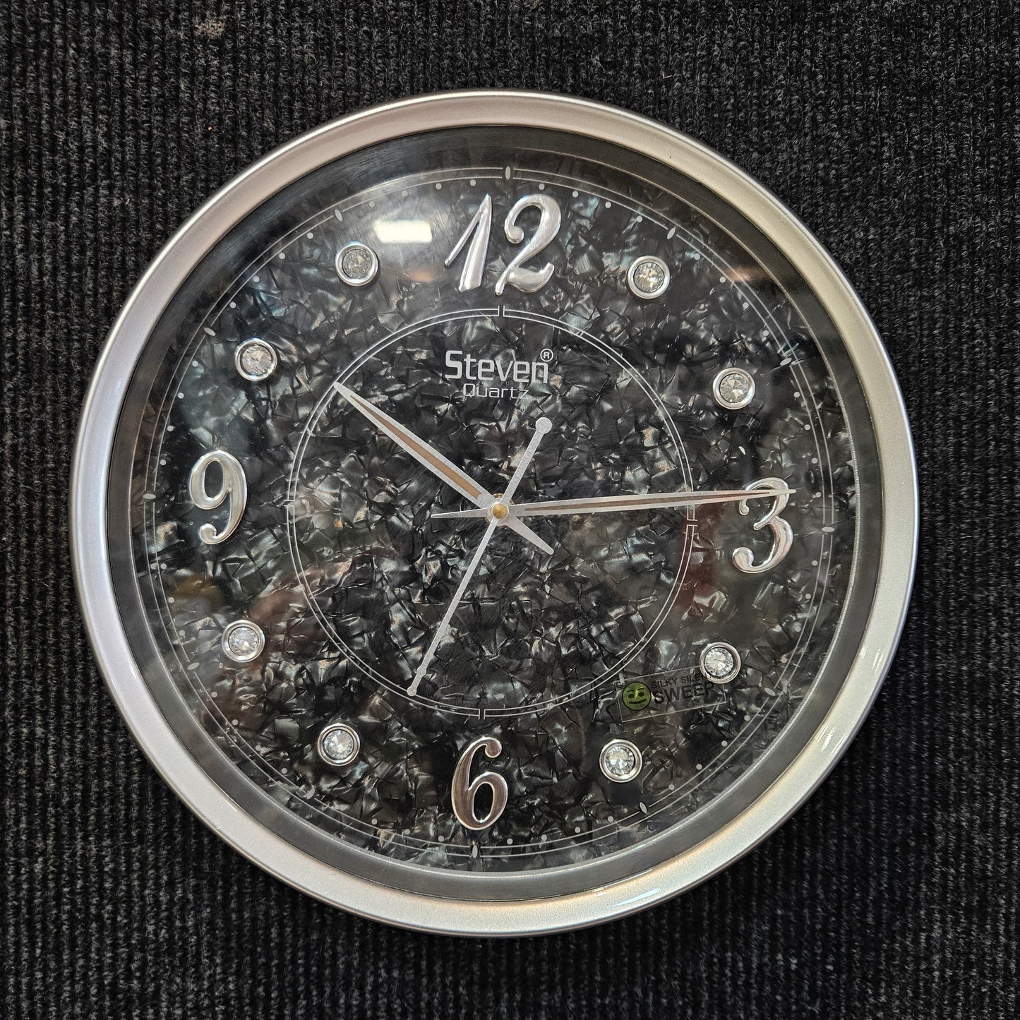 Round clock with transparent face and silver frame on a black textured background