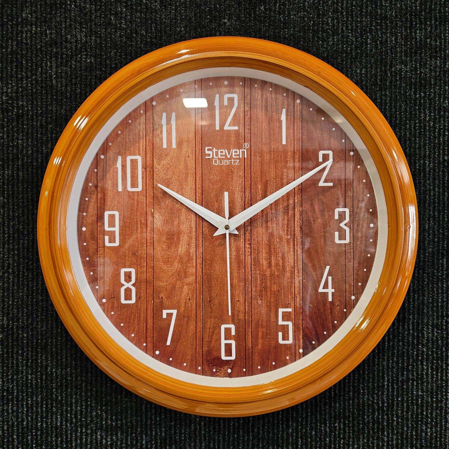 Wooden wall clock with brown face and wooden frame on a black textured background