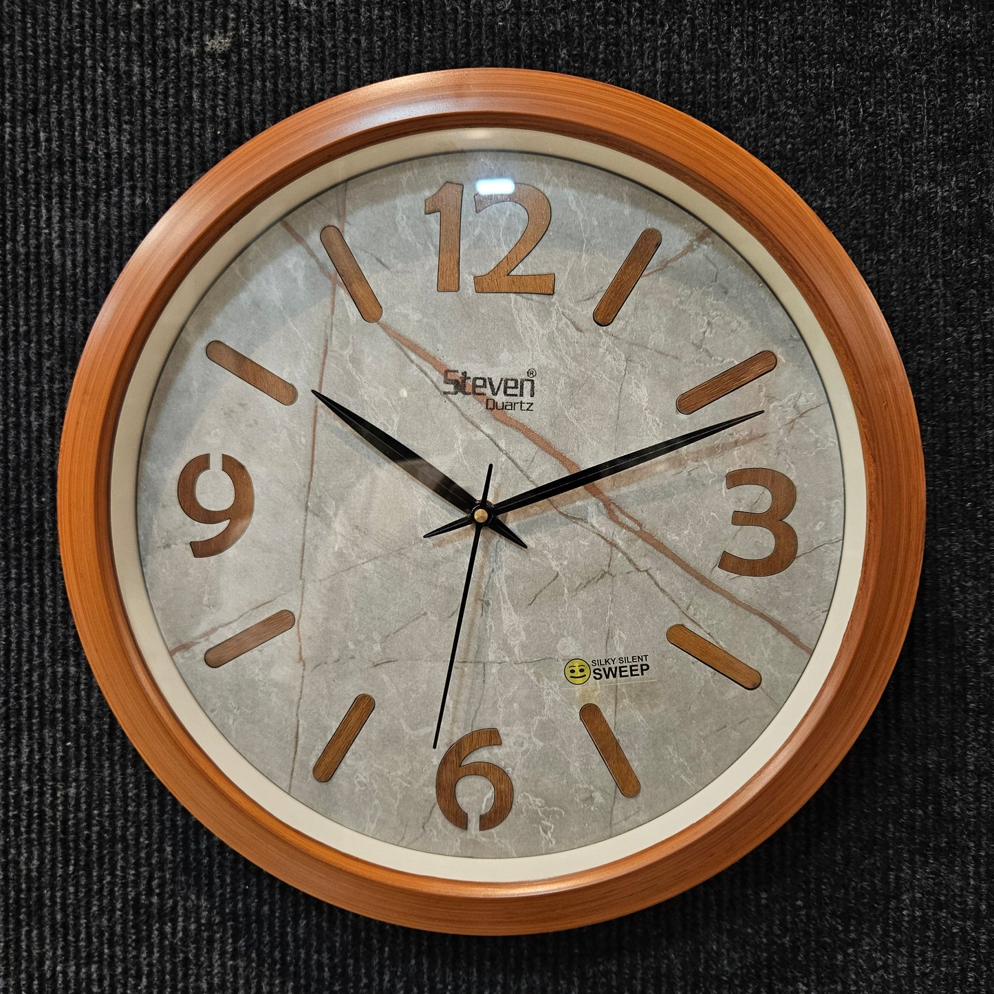 Round wall clock with wooden frame and marble-like face on a dark textured background