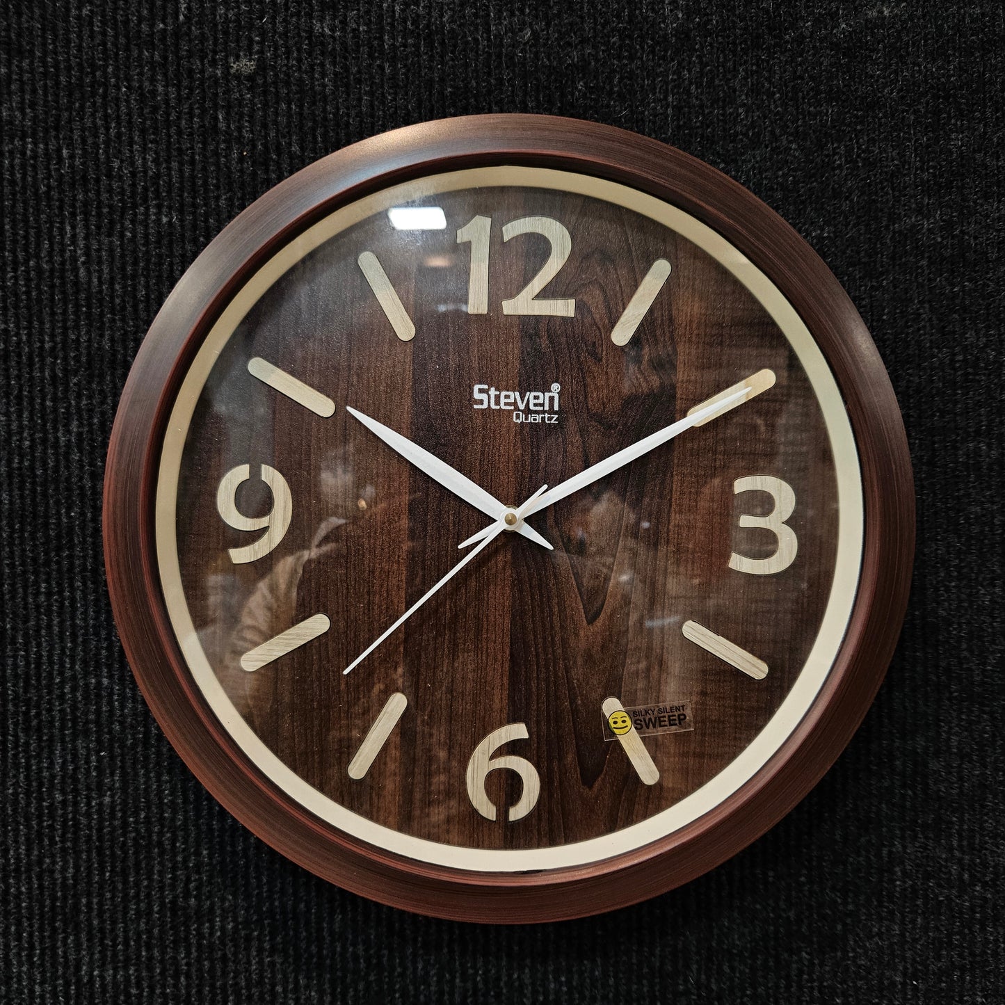 Wooden wall clock with brown frame and white numbers on a dark background