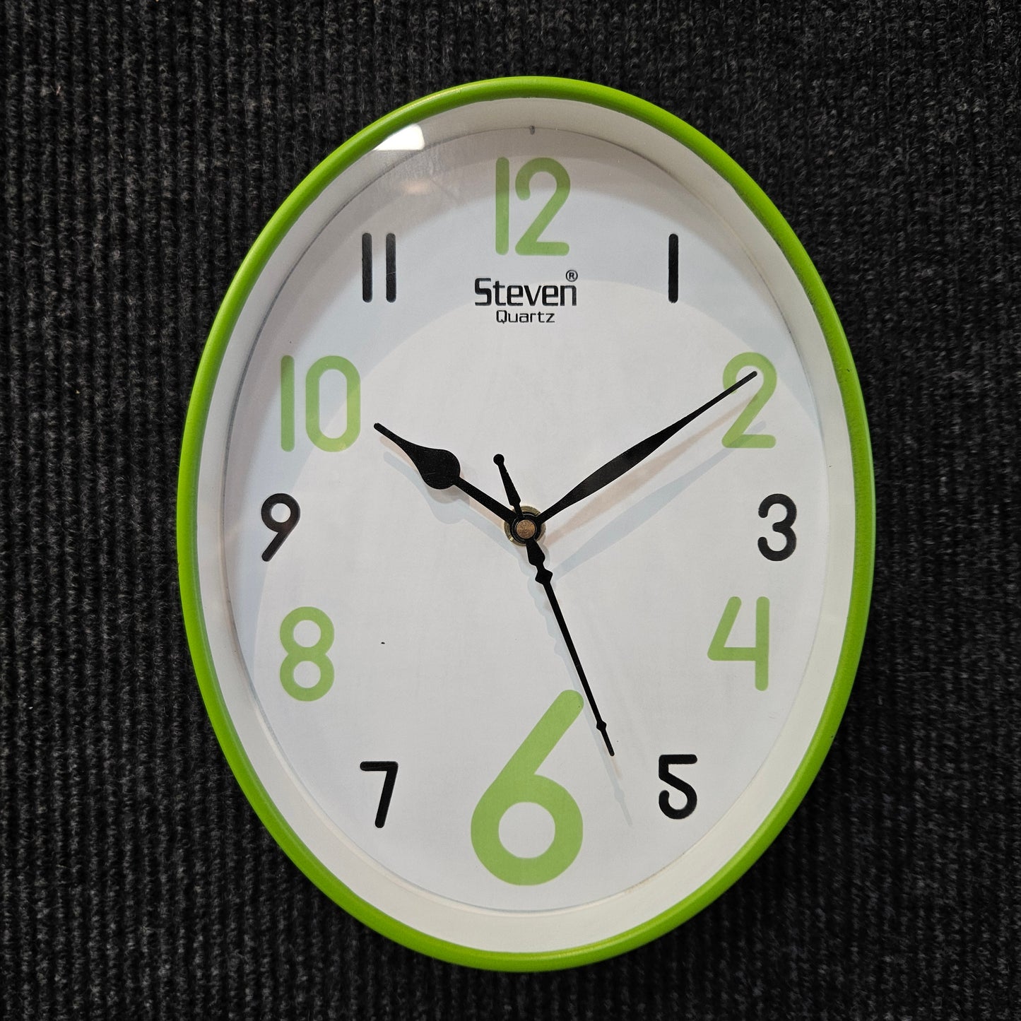 Wall clock with green frame and white face on a dark textured background