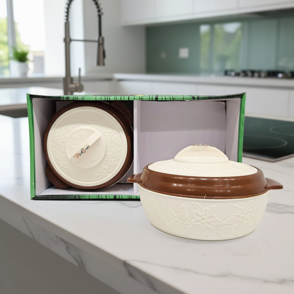 Ceramic pot with brown lid and handle on a white surface, with an open box containing another ceramic item in the background.
