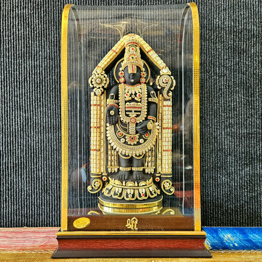 A 24 carat gold-plated statue of Lord Balaji adorned with attractive stones, displayed in a transparent protective cabin with a wooden base.