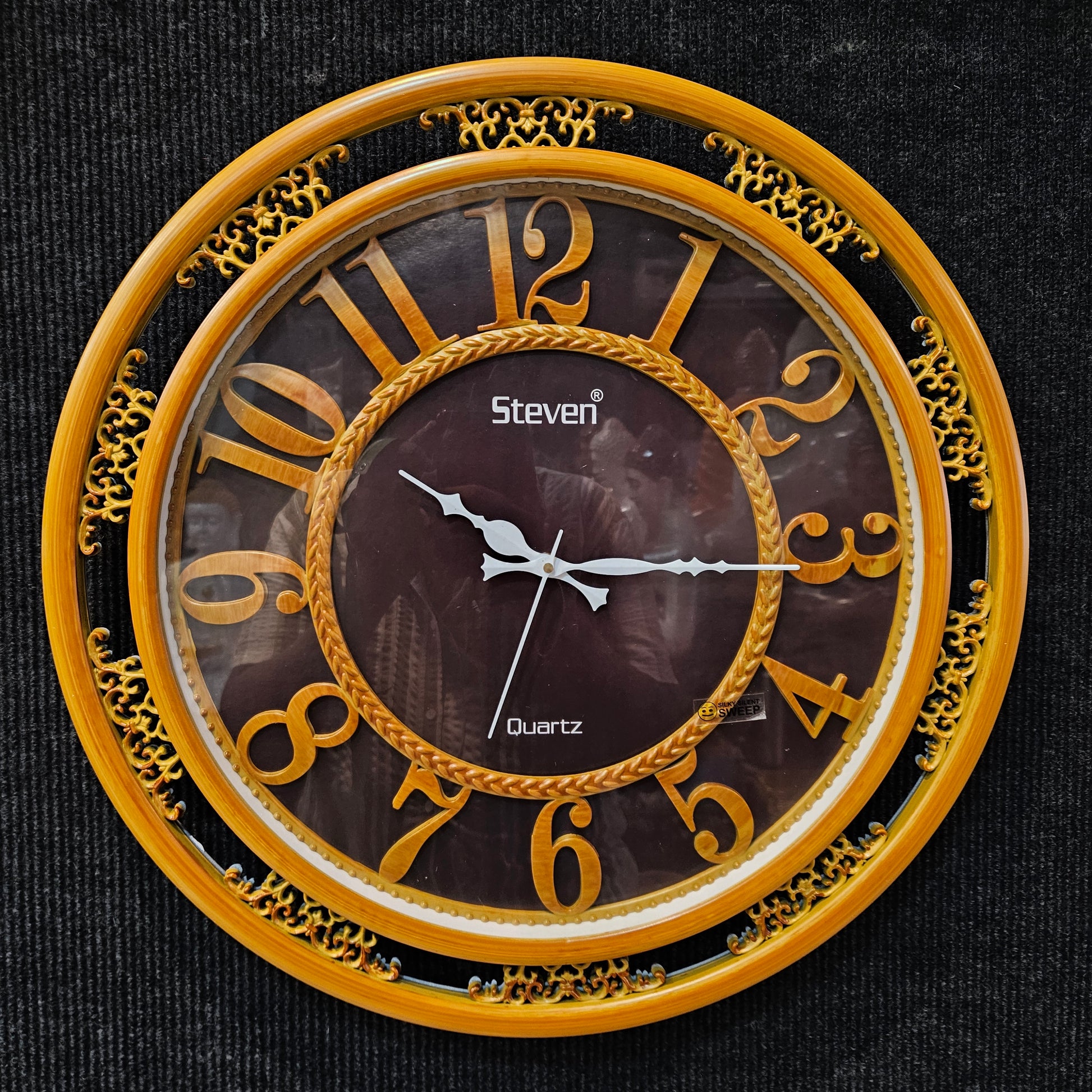 Decorative wall clock with gold frame and Roman numerals on a dark background