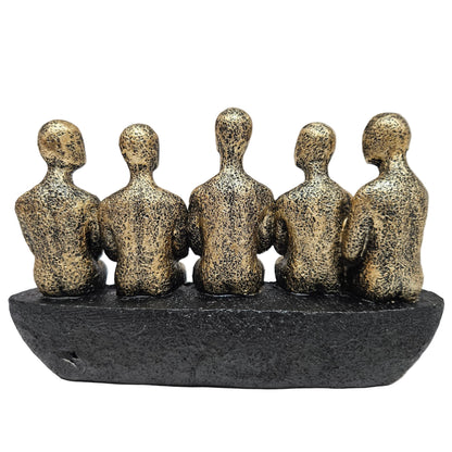 Abstract sculpture features five stylized figures seated together in a textured gold and black finish