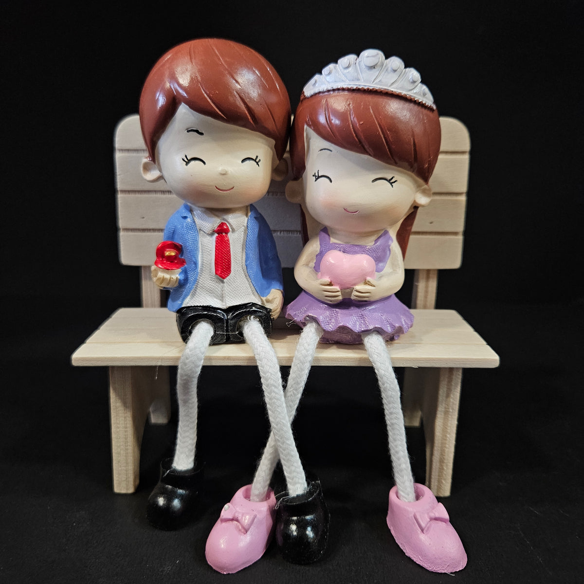 Two figurines on a small wooden platform with a black background