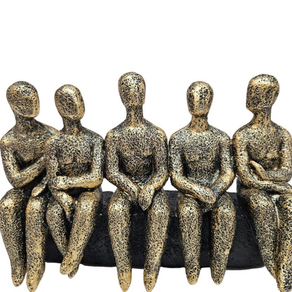 Abstract sculpture features five stylized figures seated together in a textured gold and black finish